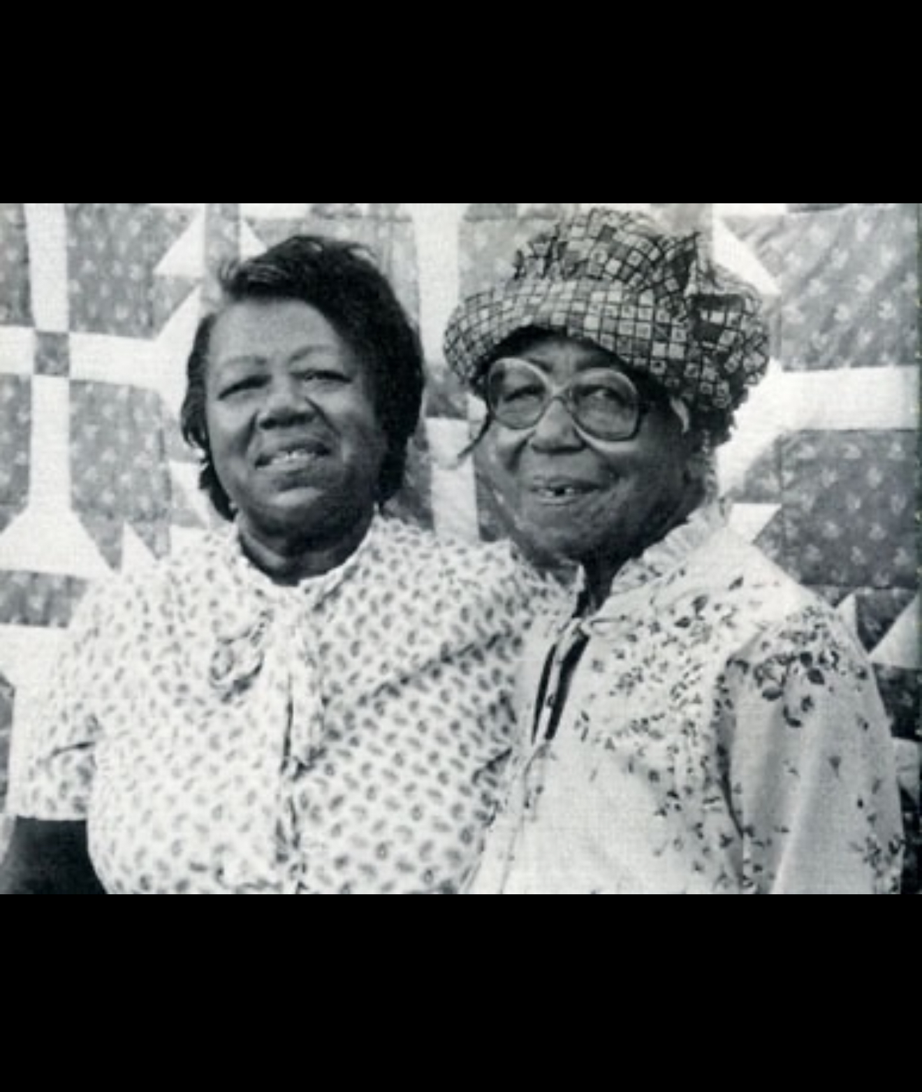 Two elders standing with a finished quilt